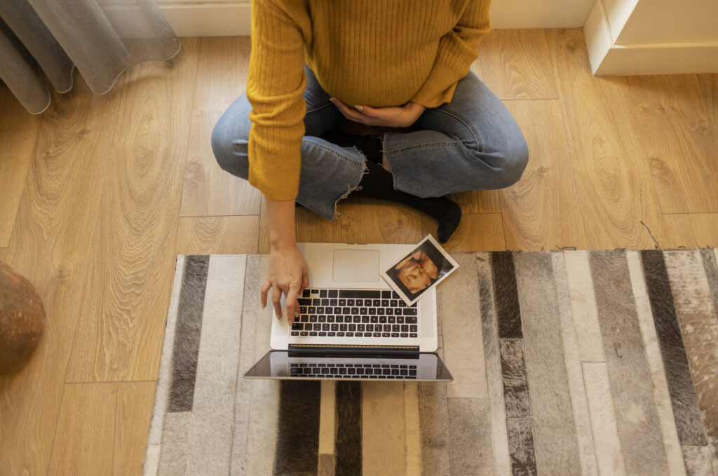 Top view of the belly of a pregnant woman with a baby ultrasound scan making a video call on the laptop with the doctor