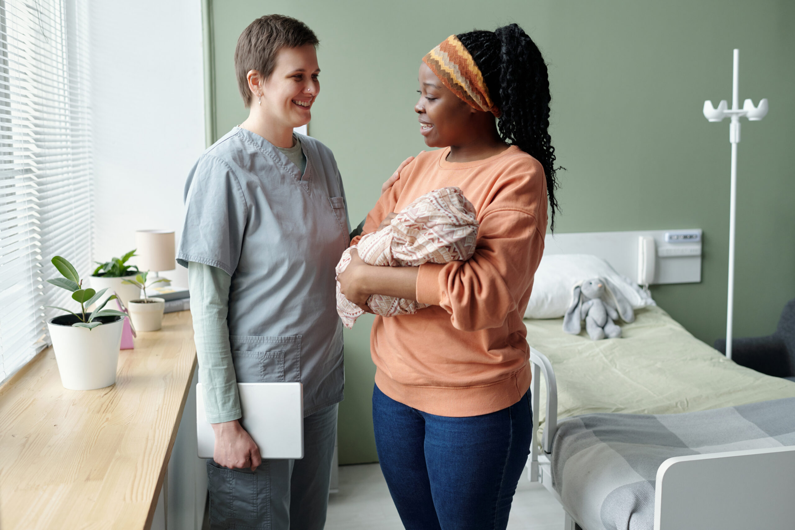 Nurse Smiling While Engaging with New Mother Holding Baby