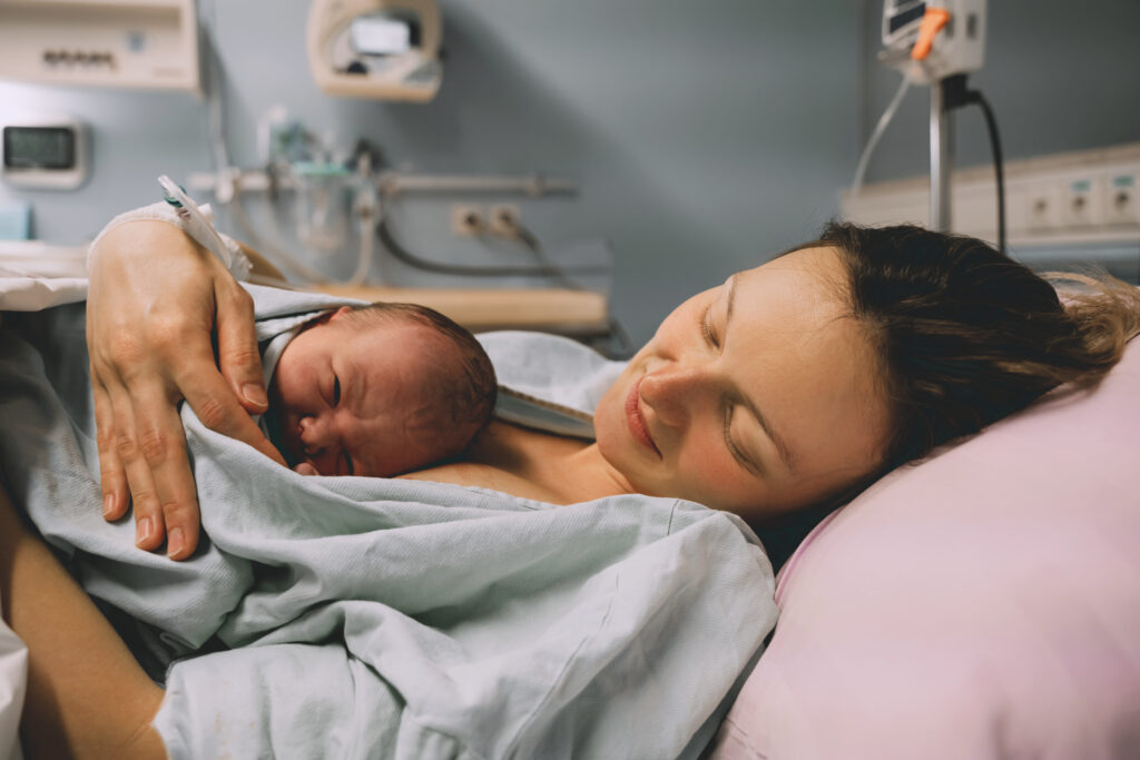 Mother and newborn. Child birth in maternity hospital. Young mom hugging her newborn baby after delivery. Woman giving birth. First moments of baby life after labor.