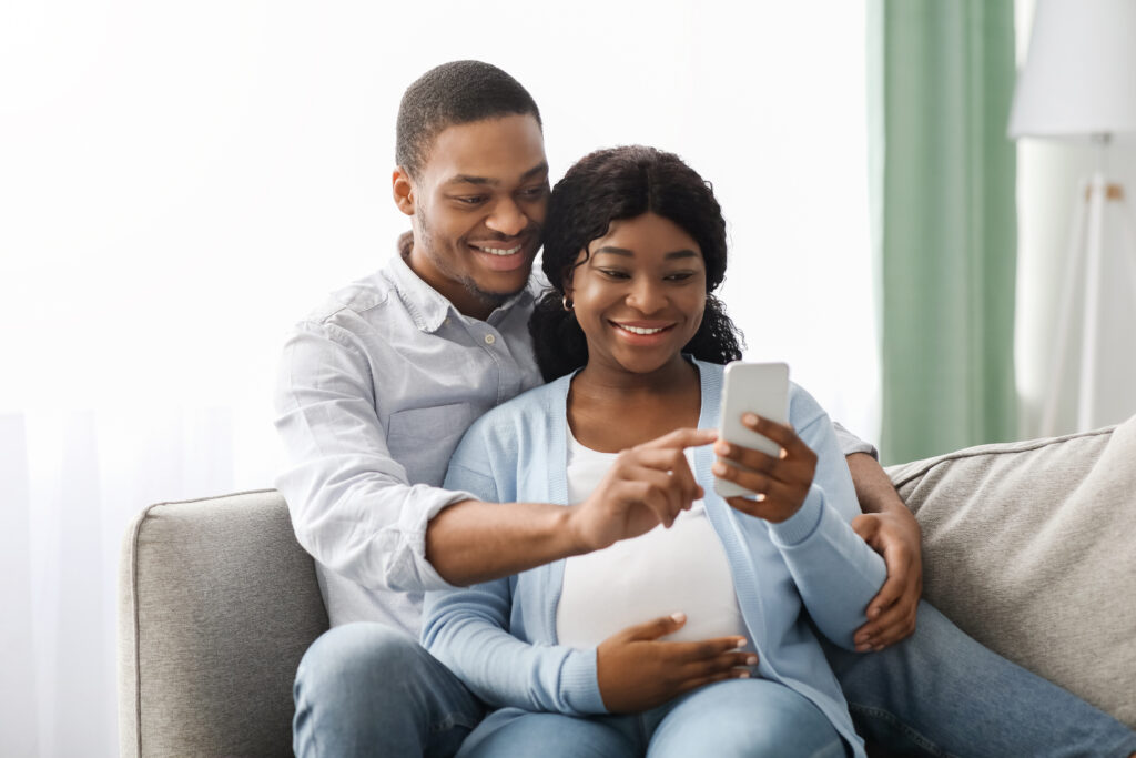 Loving black expecting parents shopping online, using smartphone